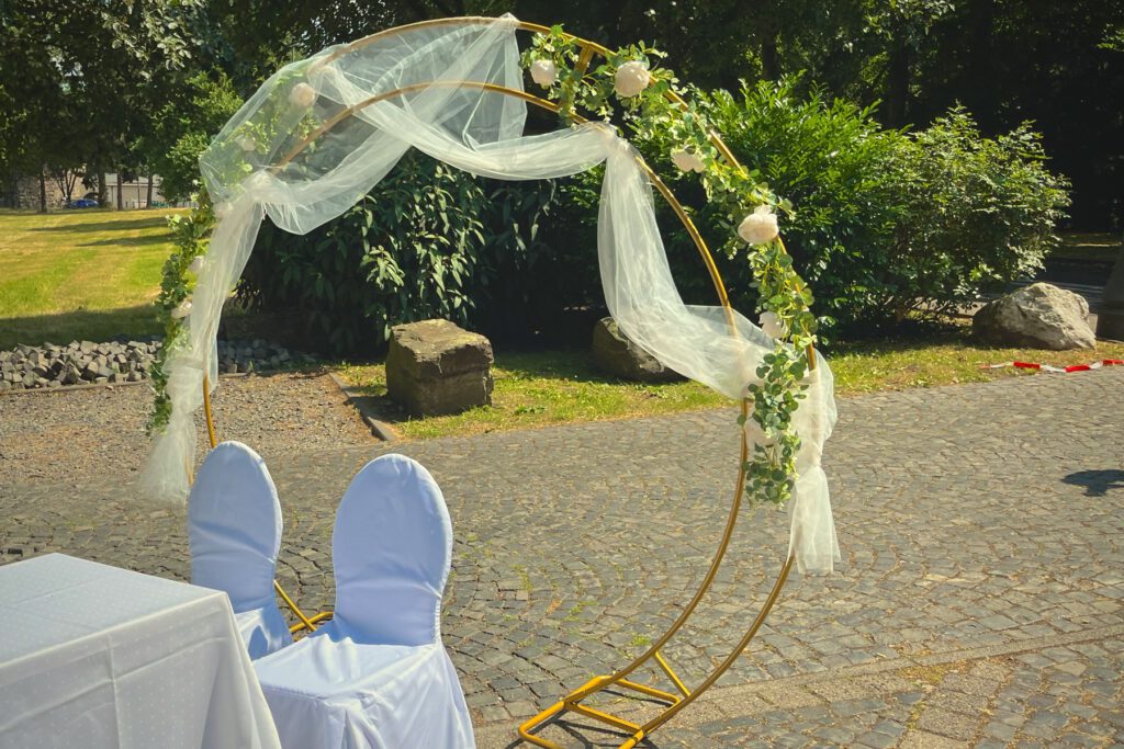 Goldener runder Traubogen mit Tüll und Blumenranke im Grünen